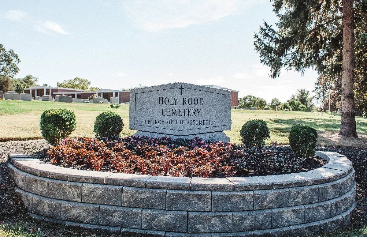 The Holy Rood Cemetery sign, set in a planted stone bed at the entrance.