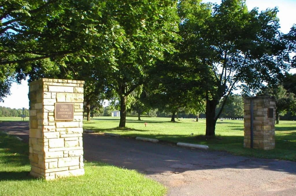 Stone entrance pillars and the tree-lined drive at Lake Nelson Memorial Park.