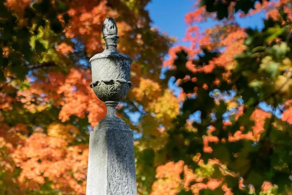 A carved stone urn atop a monument against autumn leaves at Laurel Grove Cemetery.