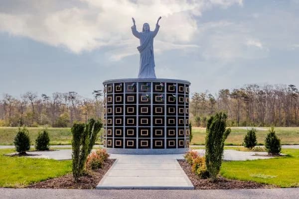A circular columbarium beneath a statue of Christ with raised arms at Resurrection Cemetery.
