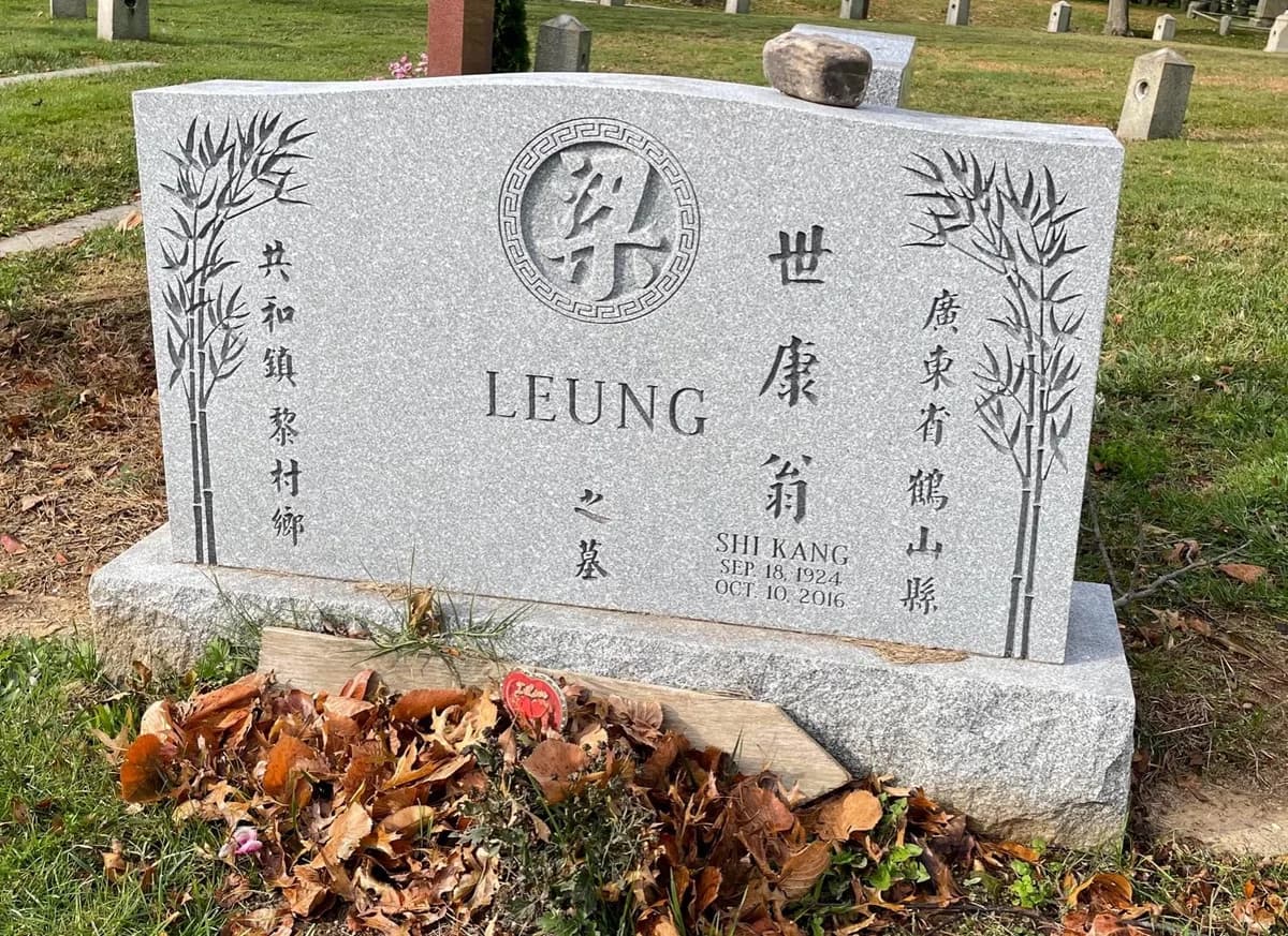 Grey granite double memorial, its family character in a carved roundel between two panels of bamboo.