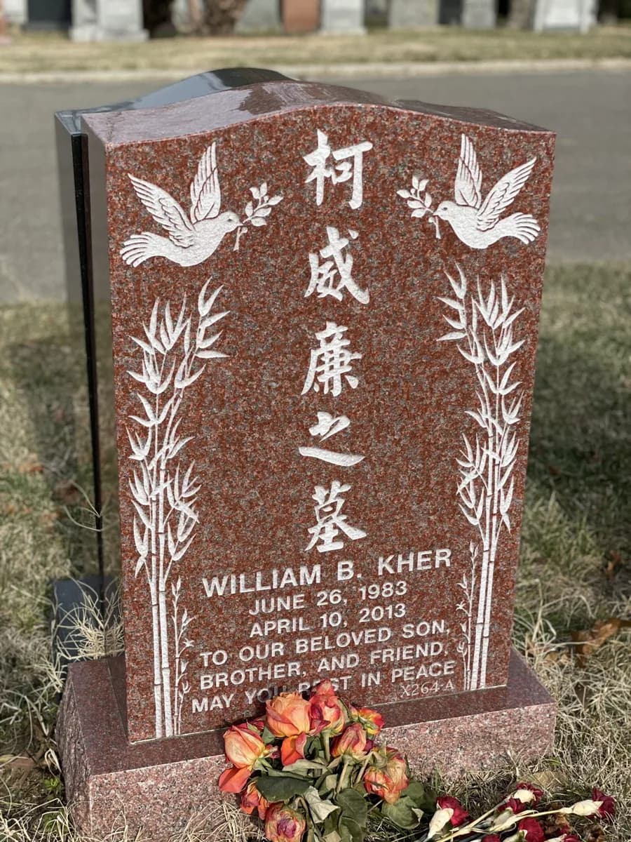Mahogany granite headstone with a stepped peaked top, a dove and bamboo carved on each side of the family name.