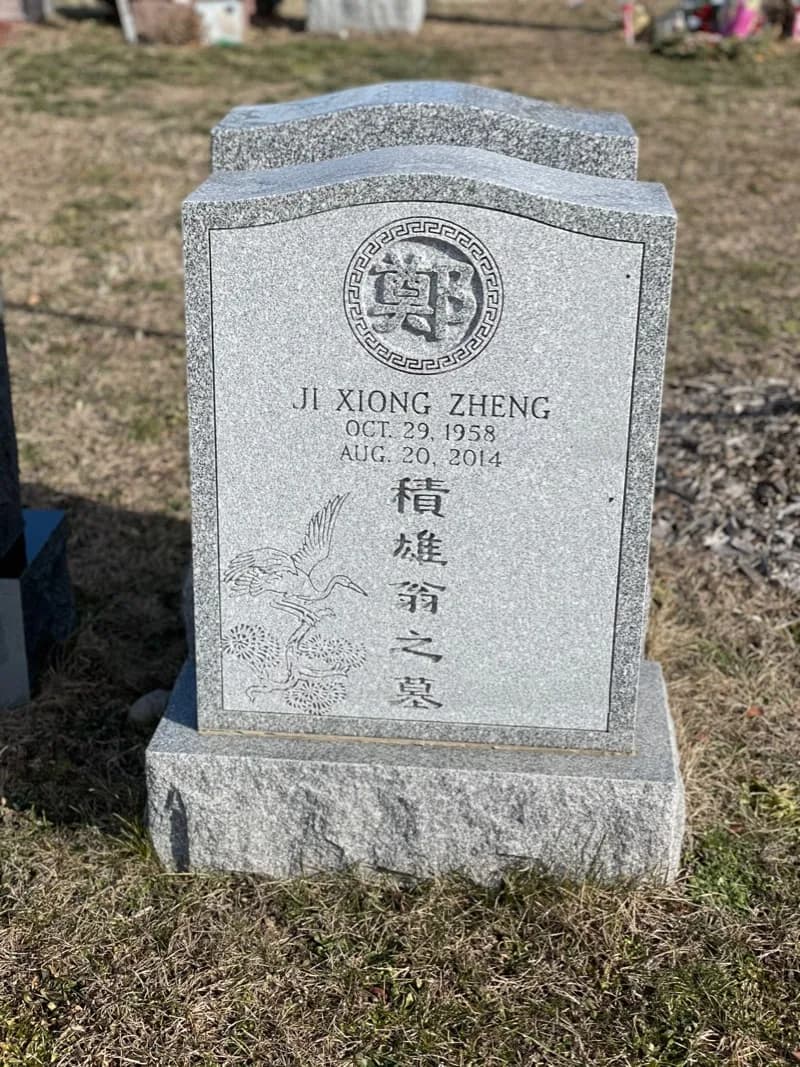 Pale granite headstone with the family character in a ringed roundel and a crane carved below the lettering, on a rock-faced base.