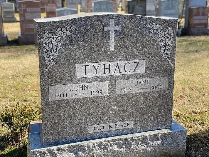 Grey granite companion headstone with a cross above two name panels and vine carving in the corners.
