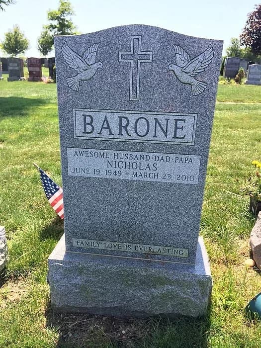 Grey granite headstone with a cross flanked by doves, on a rough-split base.